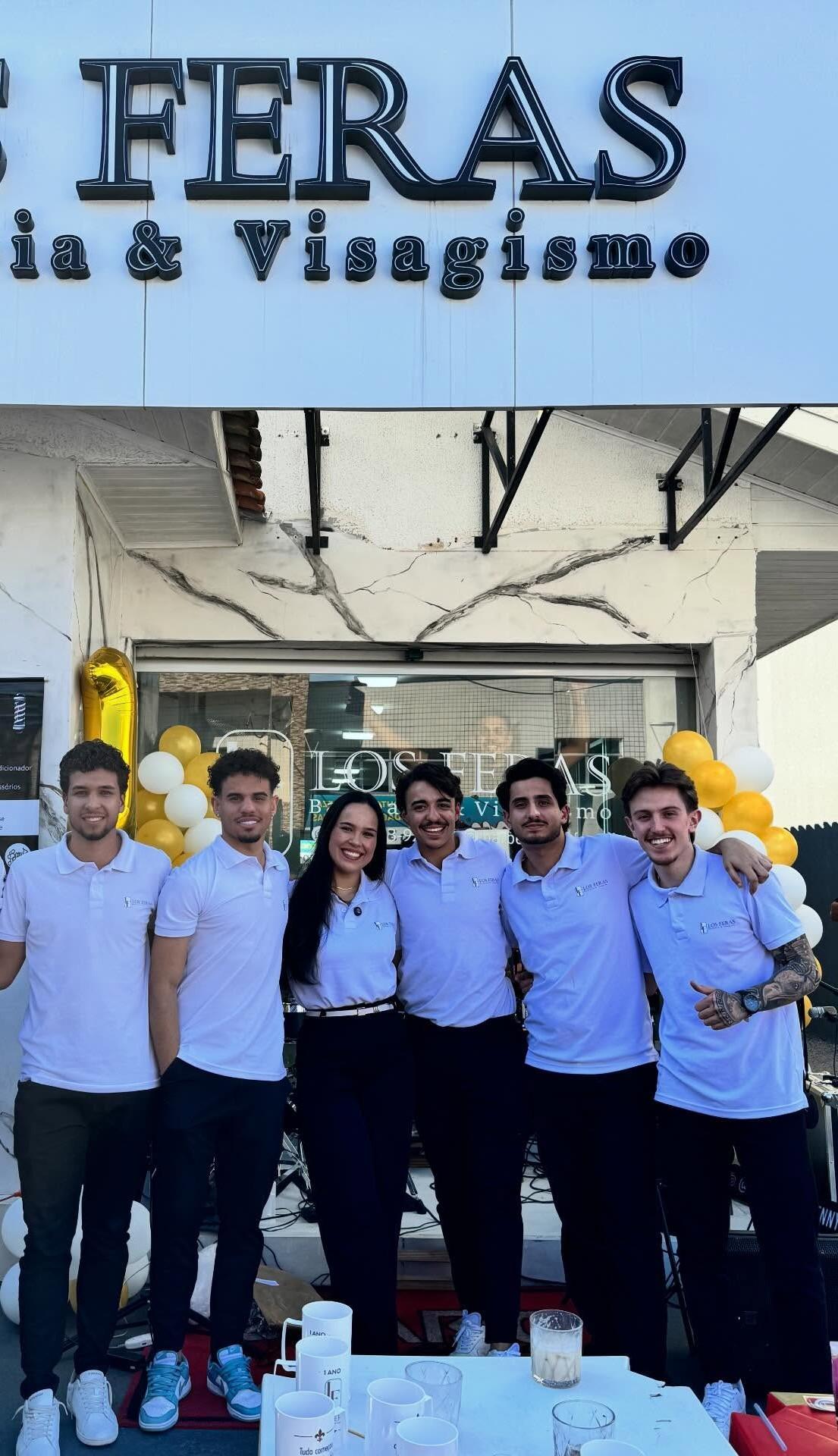 Equipe da Barbearia Los Feras reunida em frente à fachada, de camisa branca da marca