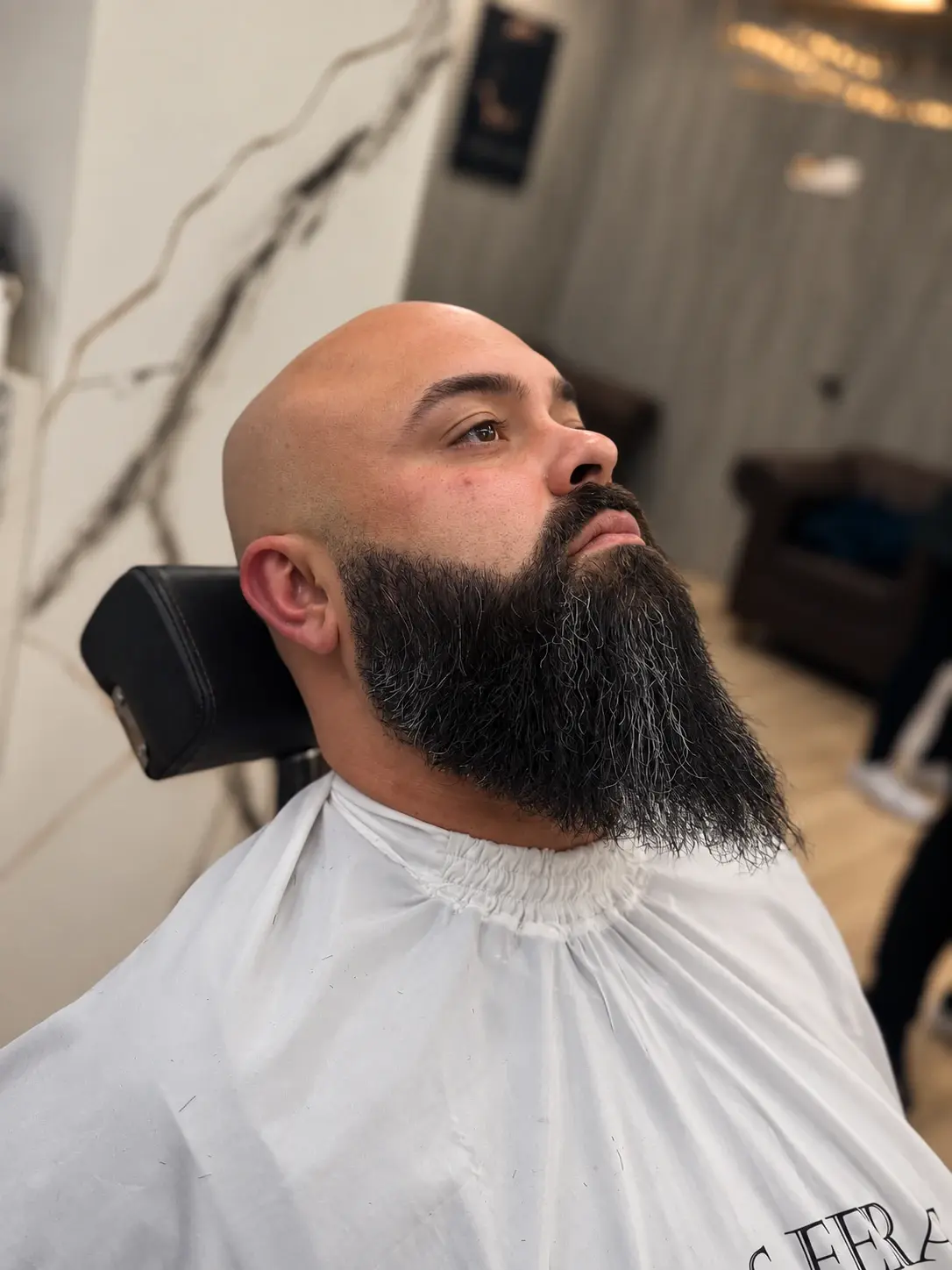 Cliente na cadeira da barbearia com a barba cheia alinhada e o contorno definido